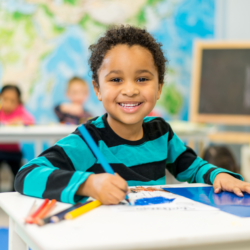 Preschool aged boy sitting at a desk smiling.